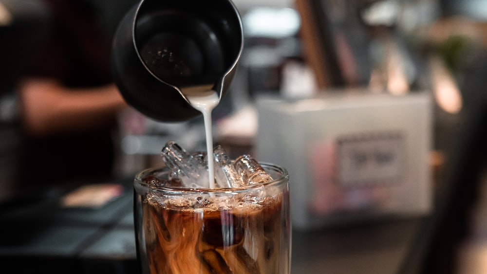 Caffeinated Delight: Barista Pouring Milk into a Glass of Iced Coffee