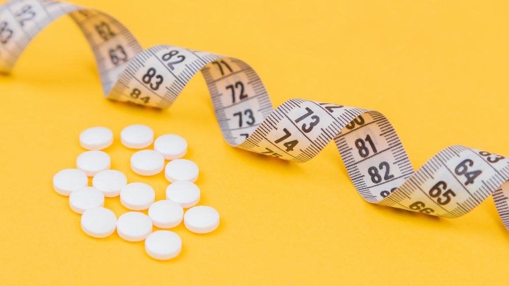 Effective Weight-Loss Tools: White Pills and Measuring Tape on Yellow Background