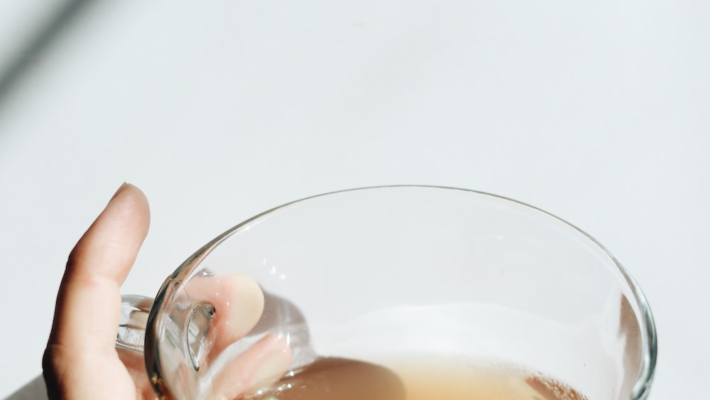 Tea: A person holding a clear drinking glass with brown liquid