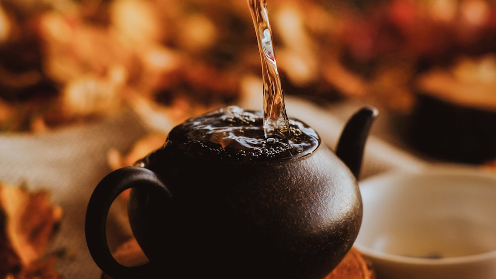 Tea Time Elegance: Black Ceramic Teapot Pouring Water into White Ceramic Teacup