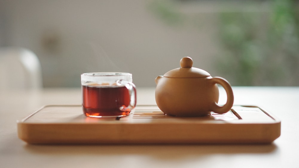Yellow Tea: A Clear Glass Cup Near Brown Ceramic Teapot